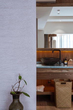 A modern bathroom with a large vessel sink, wooden accents, and a potted plant.