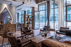 A spacious lobby with a modern design, featuring a large wooden bookshelf, leather seating, and large windows offering a view of the outdoors.