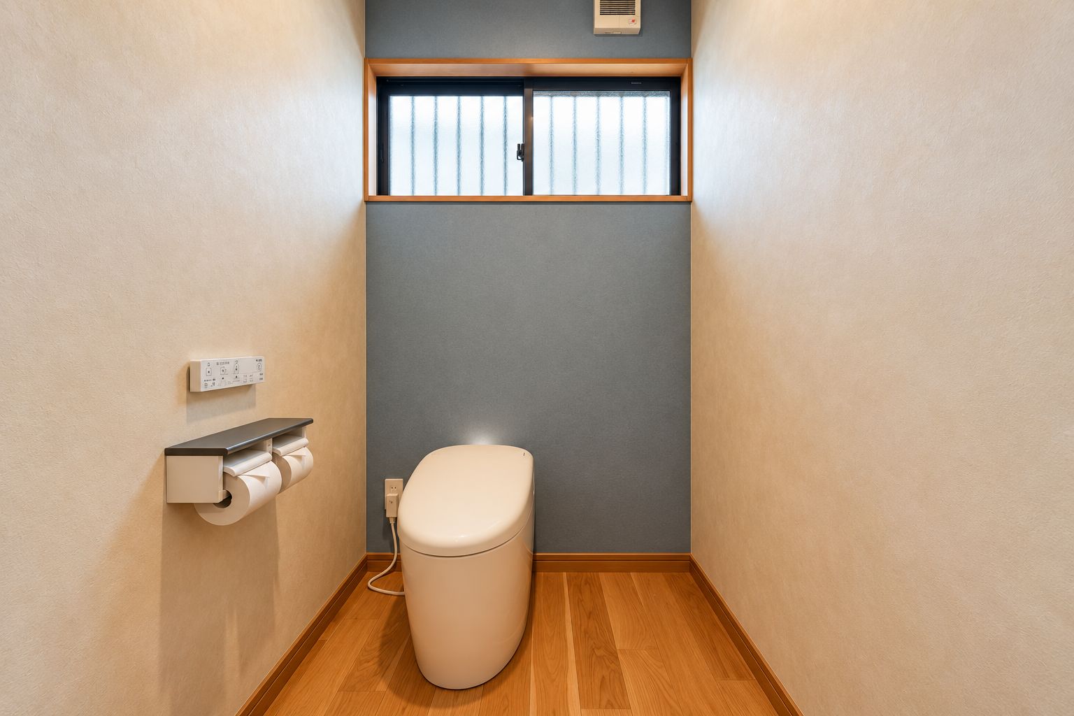 Un baño pequeño con inodoro, dispensador de papel higiénico y ventana.