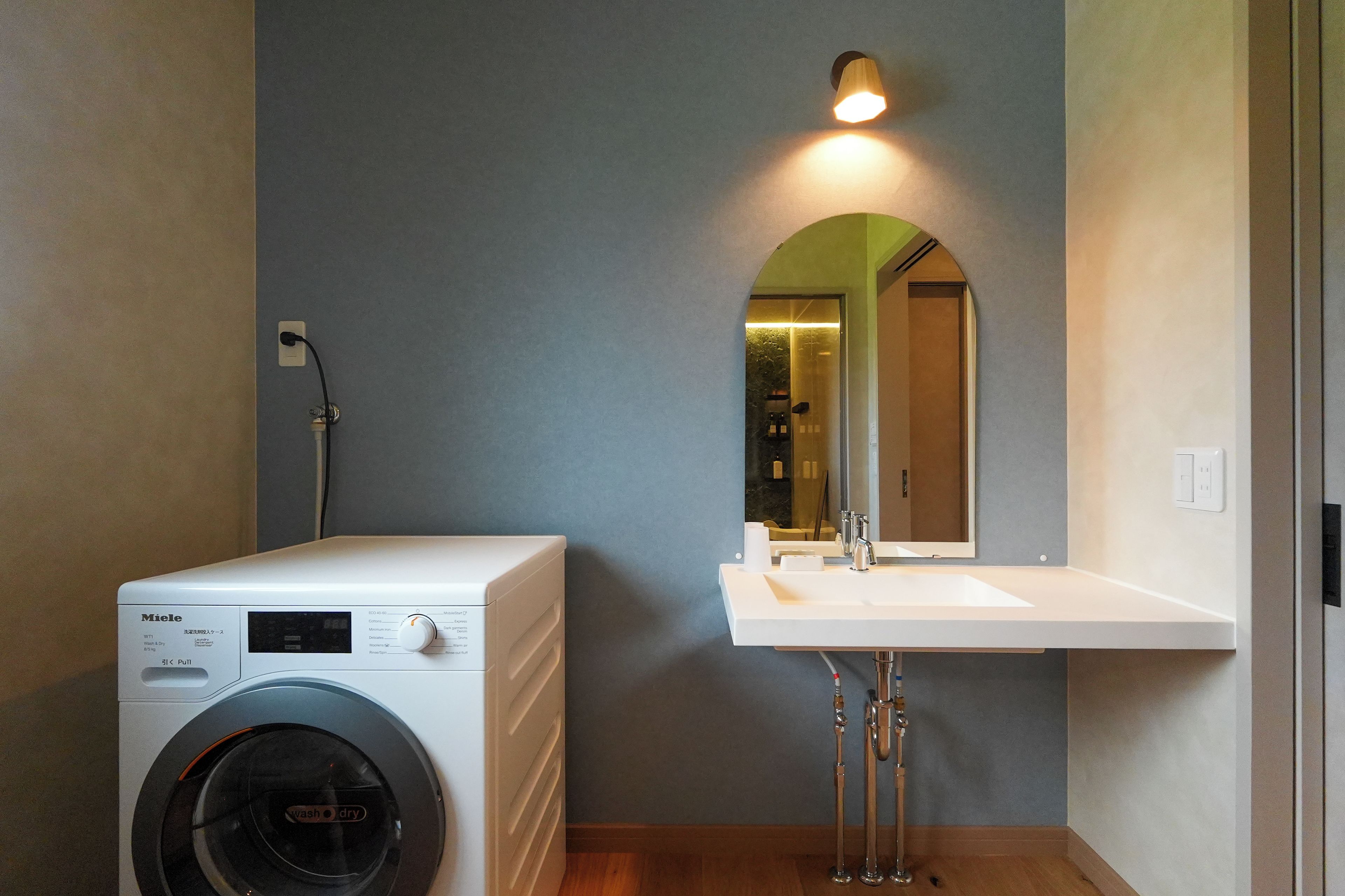 A compact bathroom with a washing machine, a sink, and a mirror.