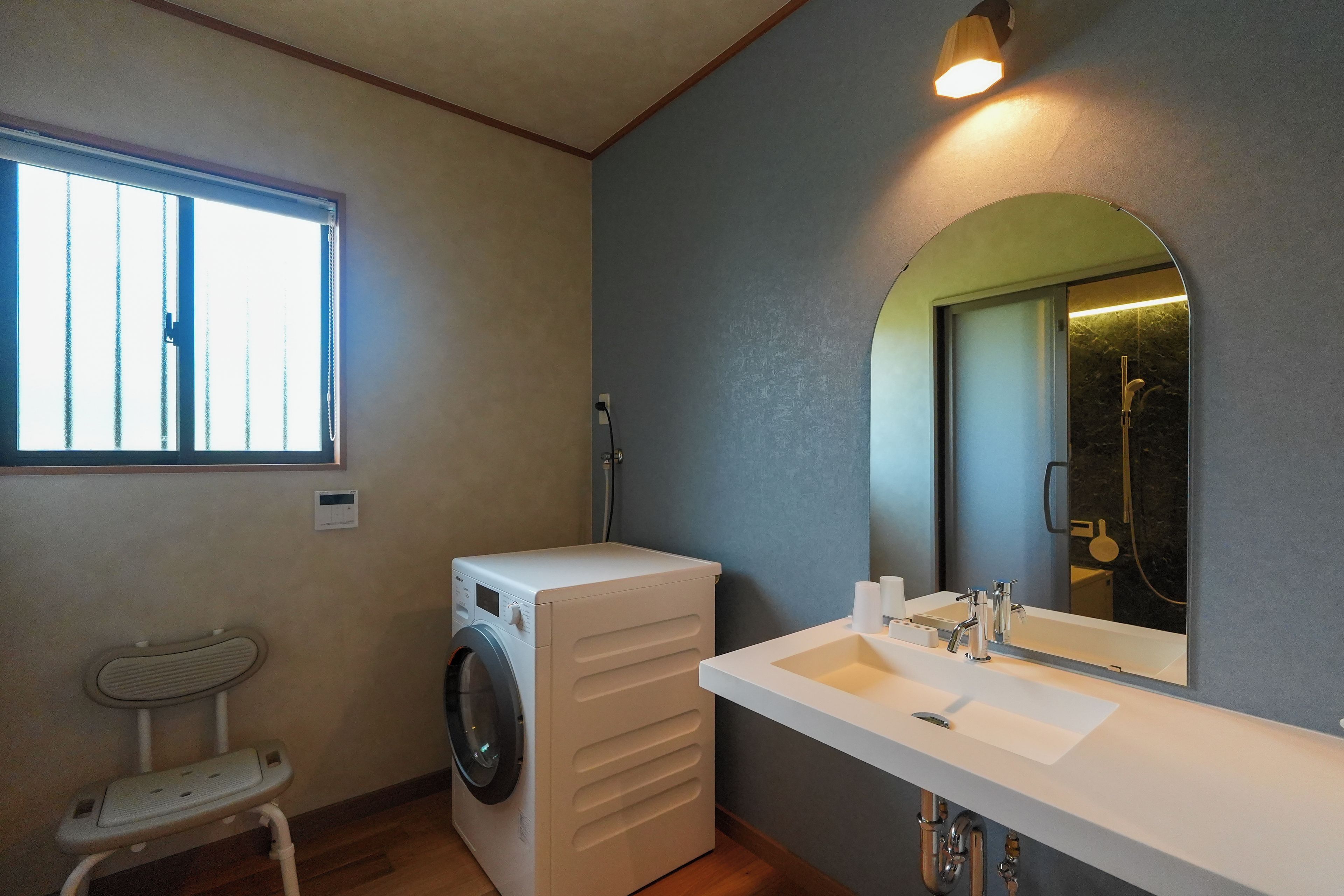 A compact bathroom with a washing machine, a sink, and a mirror.