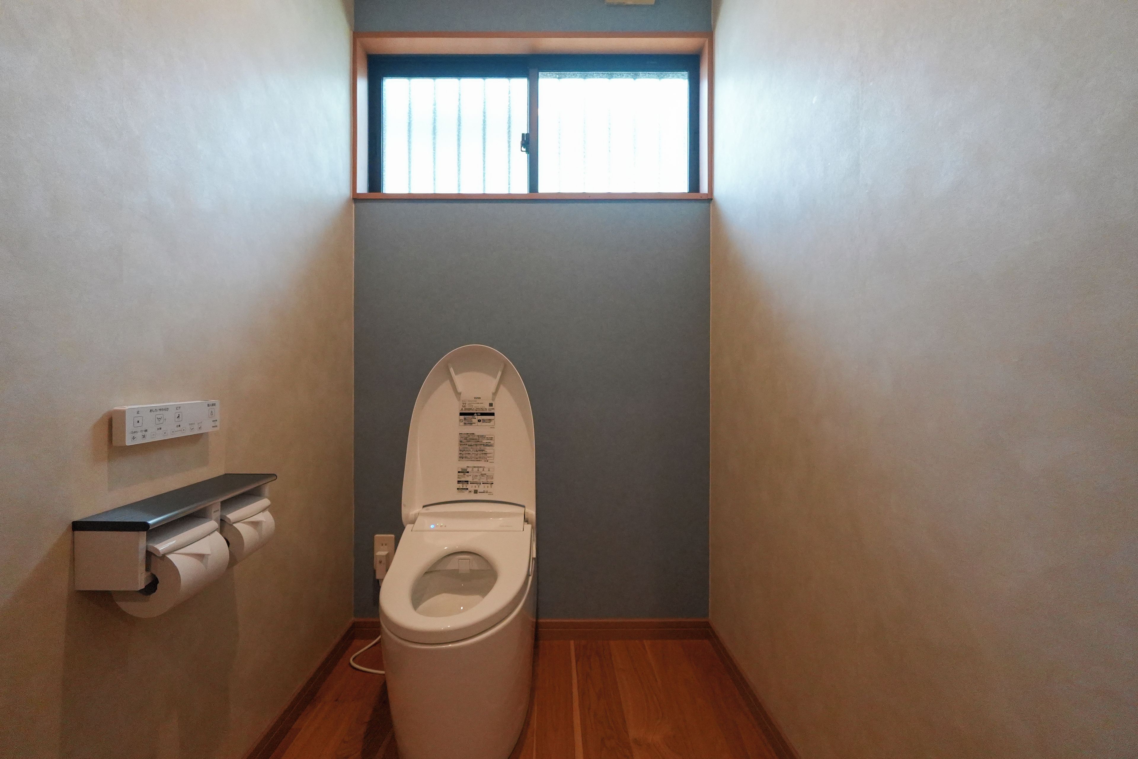 Une petite salle de bain étroite, équipée de toilettes, d’un distributeur d’essuie-tout et d’une fenêtre située au-dessus des toilettes.