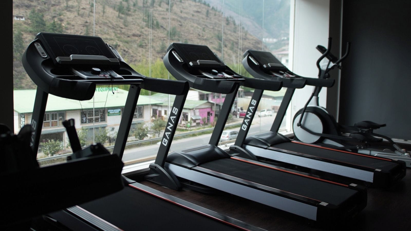 Three treadmills in a gym with a window view of a hilly landscape.
