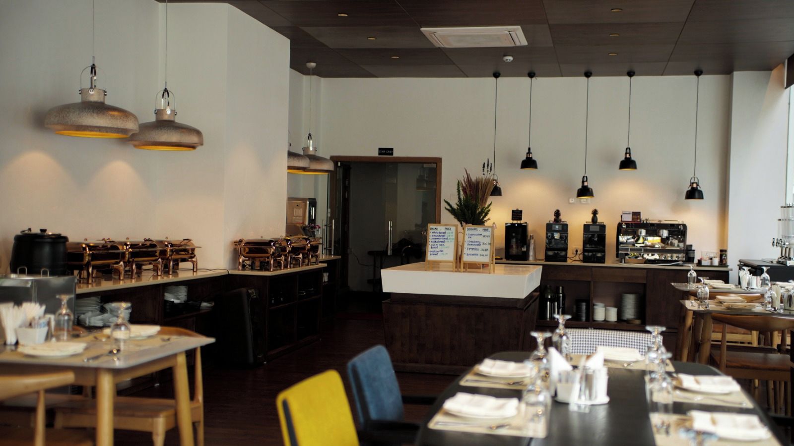 A restaurant interior with multiple dining tables, hanging pendant lights, a bar area, and a visible menu board.
