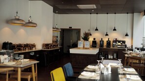 A restaurant interior with multiple dining tables, hanging pendant lights, a bar area, and a visible menu board.