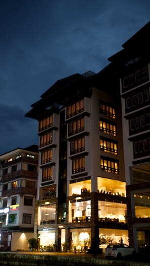 A multi-story hotel with illuminated windows and balconies, featuring a traditional architectural style with visible wooden beams and a flat roof.