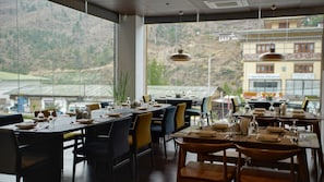 Un restaurante con mesas dispuestas para comer, ventanas amplias y vistas a un paisaje montañoso.