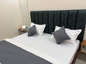A neatly made bed with a dark headboard, white pillows, and a grey quilted throw. - The Gita Ashraya Sadan Guest House (Vrindavan)