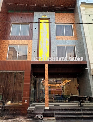 Un edificio con una entrada destacada, un letrero vertical con diseño floral y el nombre 'GITA ASHRAYA SADAN' exhibido sobre la entrada.