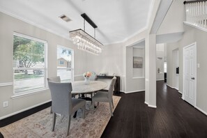 A modern dining area with a marble table, grey upholstered chairs, and a decorative chandelier. - Dream Oasis – Spacious 5BR w/ Outdoor Kitchen Katy TX (Katy)
