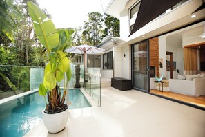 A modern outdoor pool area with a potted plant, a glass-enclosed seating area, and a view of the surrounding greenery. - Luxury Rainforest Retreat | Private 20m Pool | Walk to Beach and Shops | Suffolk (Suffolk Park)