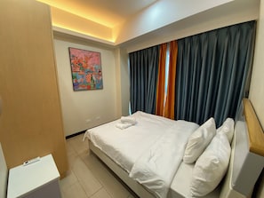 A hotel room with a bed, a painting on the wall, and a window with curtains. - Seaview 1BR  2BR 3BR Next Okada (Parañaque)