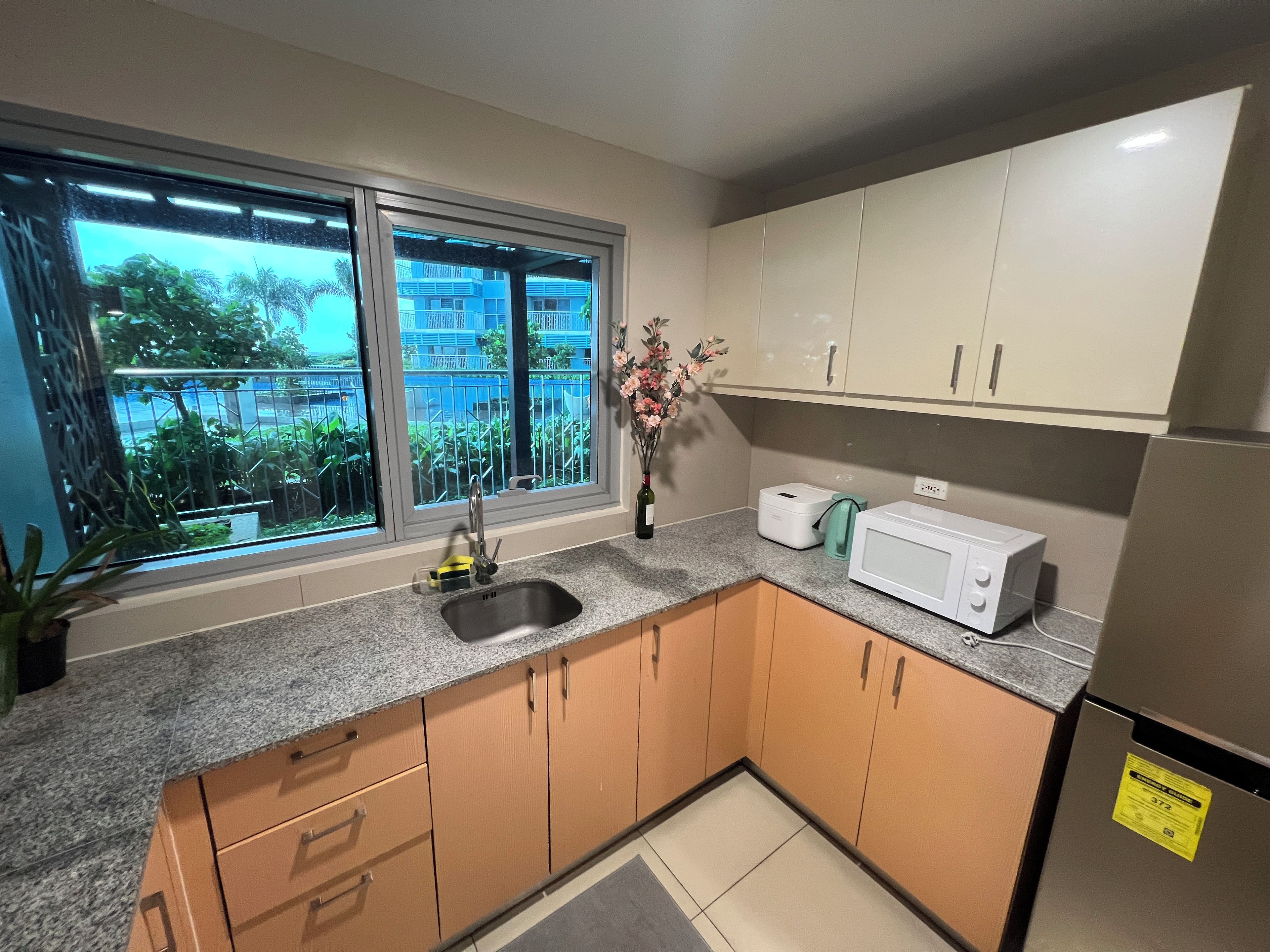Una cocina con ventana, un lavamanos, armarios, un microondas y un refrigerador.