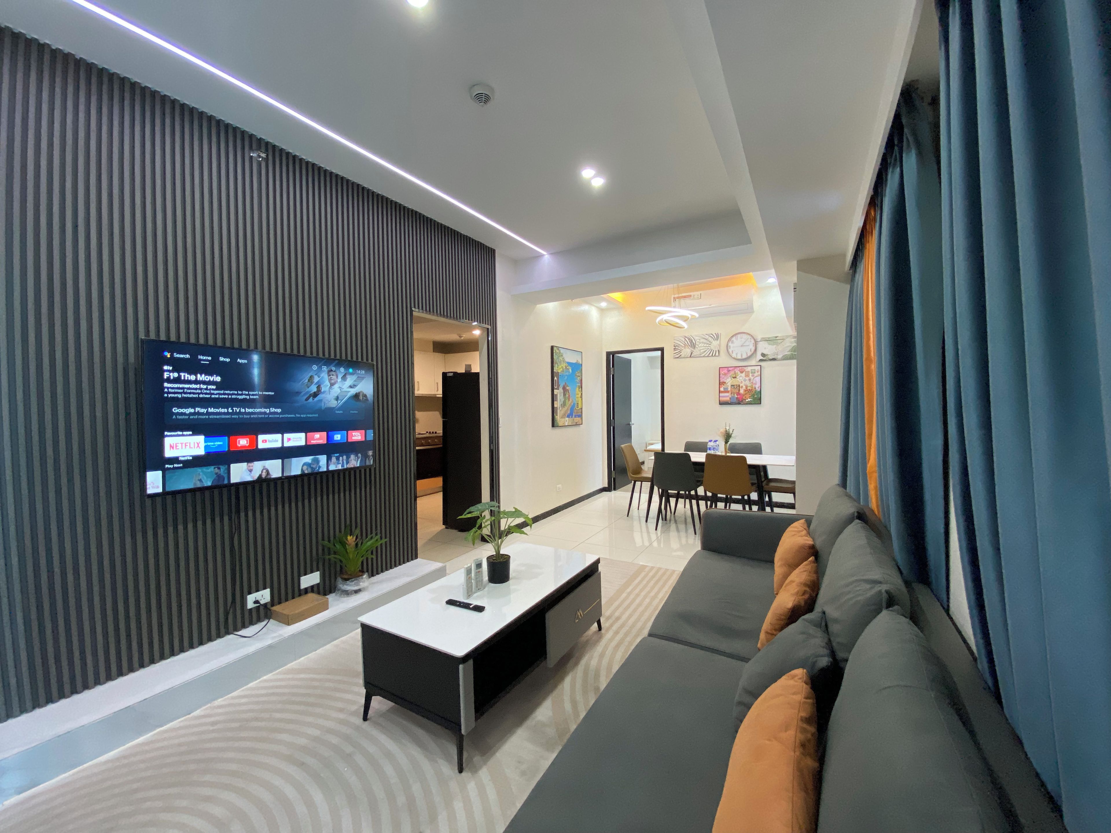 Una sala moderna con un televisor de pantalla plana montado en la pared, un sofá, una mesa de centro y un comedor con sillas y una mesa.