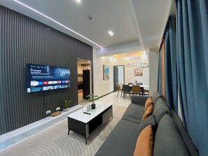 A modern living room with a flat-screen TV mounted on a wall, a sofa, a coffee table, and a dining area with chairs and a table. - Seaview 1BR  2BR 3BR Next Okada (Parañaque)