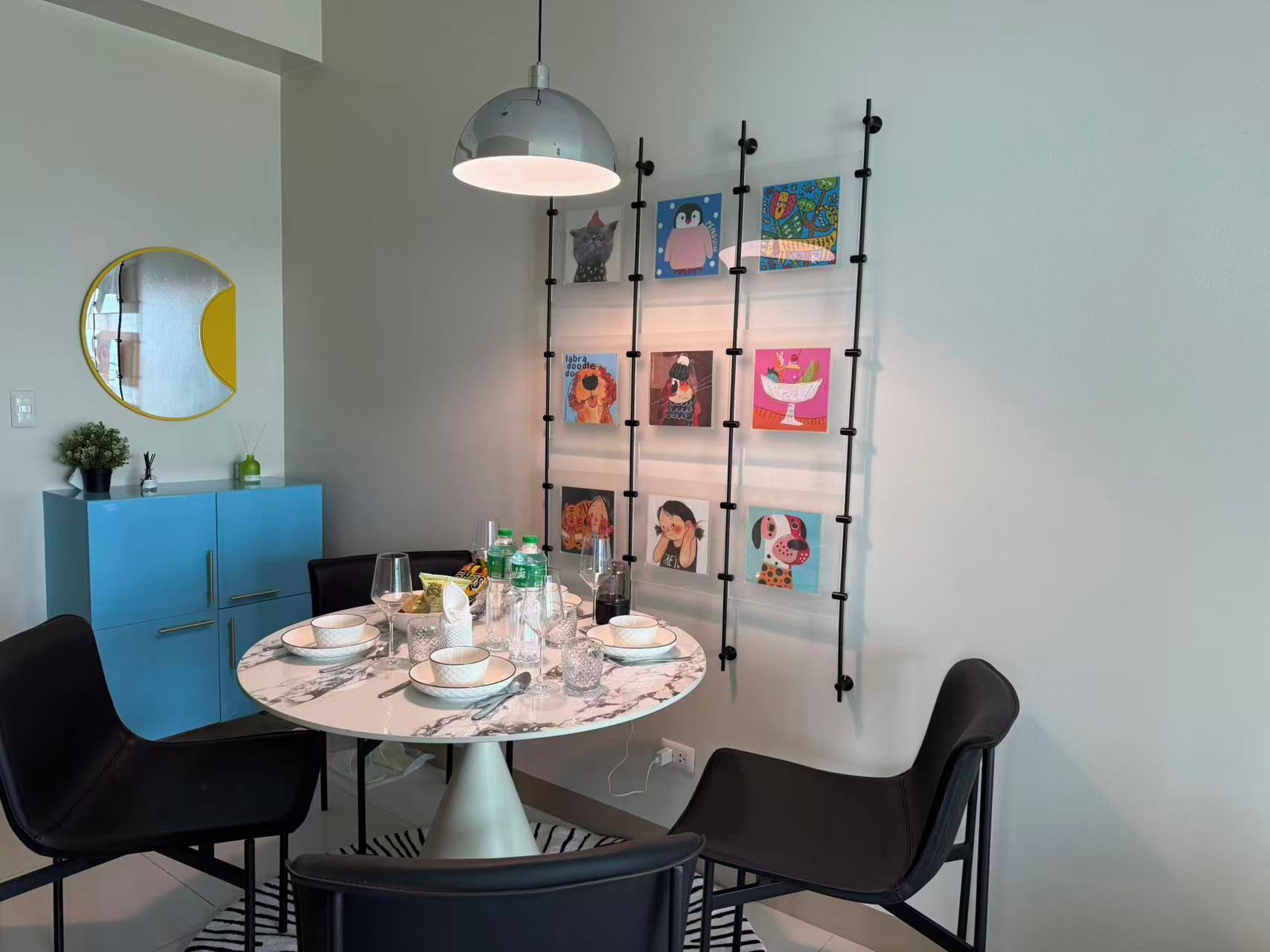 Un coin repas avec une table ronde dressée pour quatre personnes, un buffet bleu et une œuvre d’art accrochée au mur.