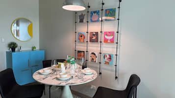 Un coin repas avec une table ronde dressée pour quatre personnes, un buffet bleu et une œuvre d’art accrochée au mur.