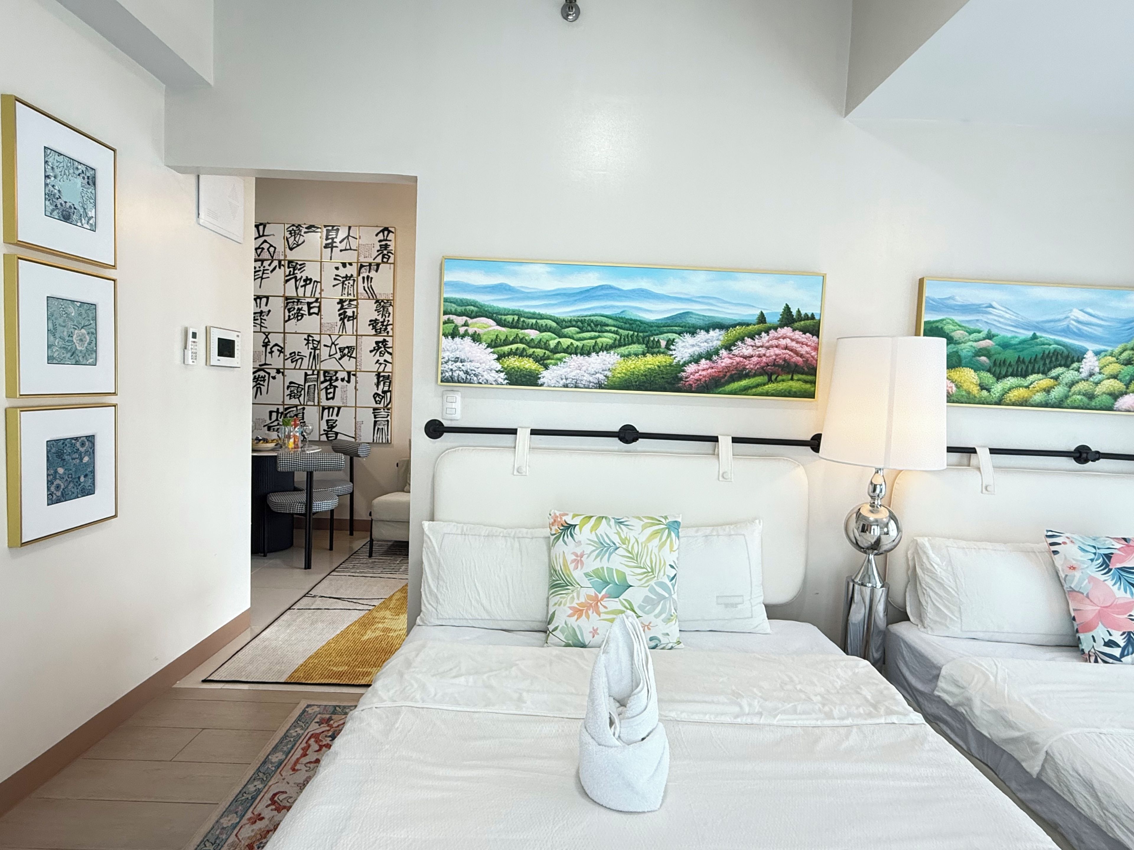 A hotel room with a bed, a bedside table, a lamp, and a painting of a landscape.
