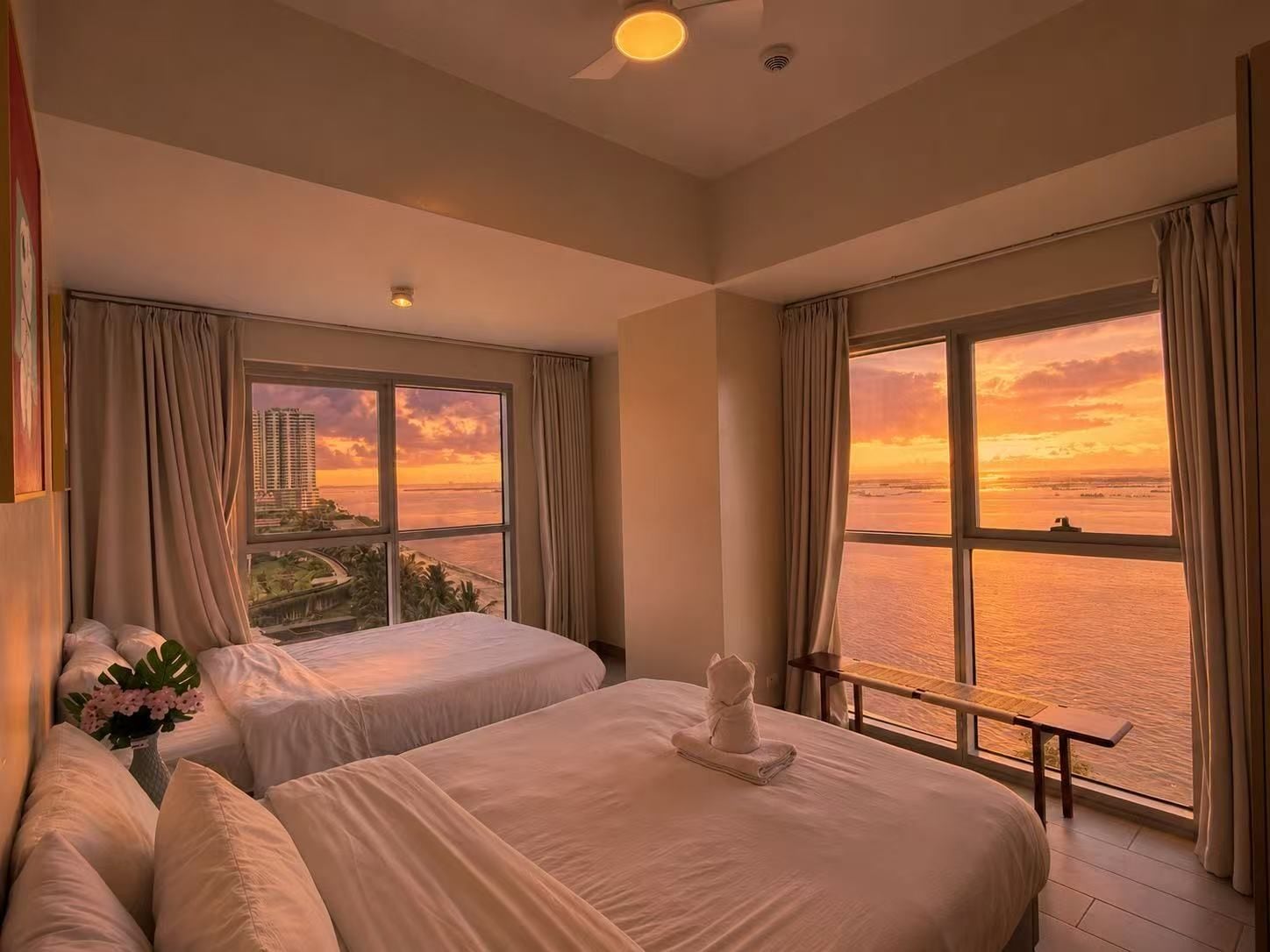 Habitación de hotel con dos camas, vista al mar y al paisaje urbano.