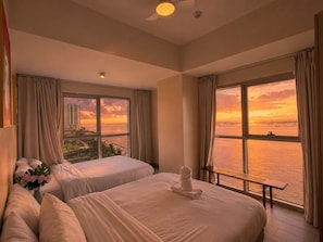 Habitación de hotel con dos camas, vista al mar y al paisaje urbano.