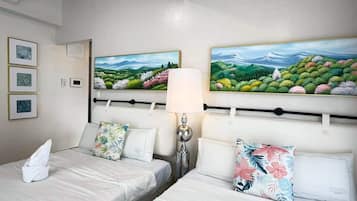 Une chambre d’hôtel avec deux lits, une table de chevet, une lampe et deux tableaux accrochés au mur.