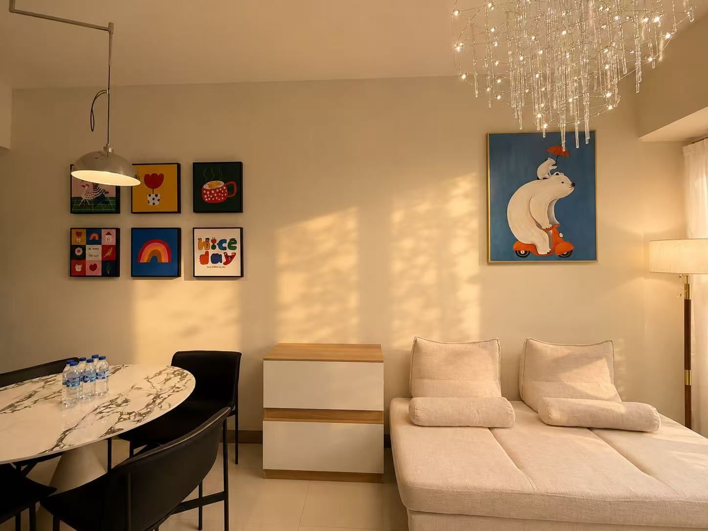 Un salon moderne comprenant un canapé, une table à manger avec des chaises, un lustre et diverses œuvres d’art murales.