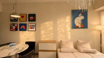 Un salon moderne comprenant un canapé, une table à manger avec des chaises, un lustre et diverses œuvres d’art murales.