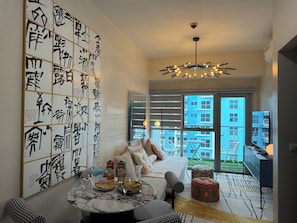 Una sala de estar moderna con una gran pared de caligrafía, un comedor con una mesa dispuesta para dos personas y vistas a un edificio azul a través de amplias ventanas.
