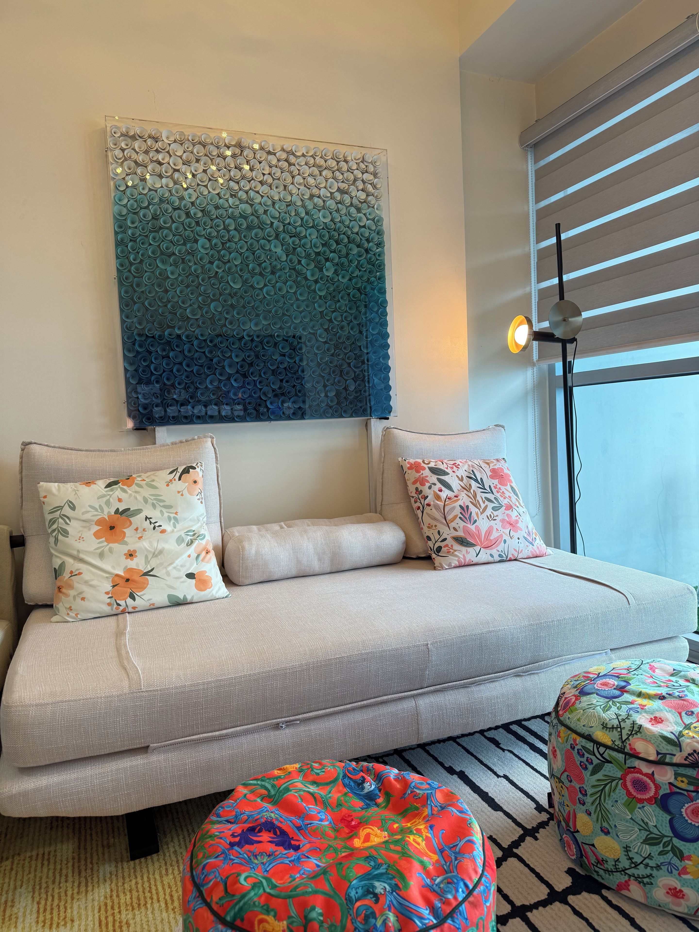 A modern living room with a sofa, decorative pillows, a colorful ottoman, and a wall art piece.