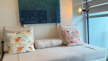 A modern living room with a sofa, decorative pillows, a colorful ottoman, and a wall art piece.