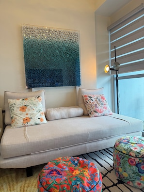 A modern living room with a sofa, decorative pillows, a colorful ottoman, and a wall art piece. - Seaview 1BR  2BR 3BR Next Okada (Parañaque)