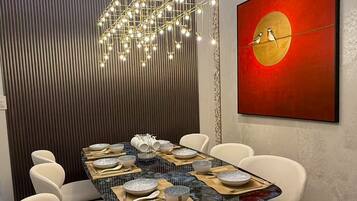 Een moderne eetruimte met een tafel met glazen blad, witte stoelen en een hanglamp.
