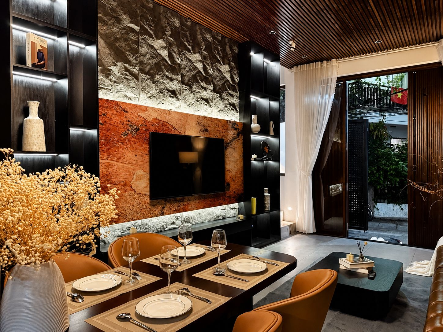 A modern dining area with a stone accent wall, a flat-screen TV, and a view of a staircase.