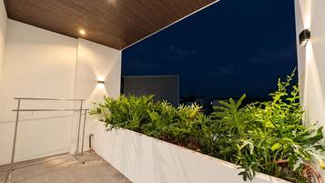 An outdoor balcony with a metal drying rack, a white planter with green plants, and a night sky.