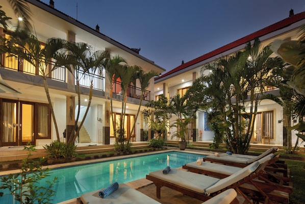 A hotel with a swimming pool, palm trees, and a red-roofed building.
