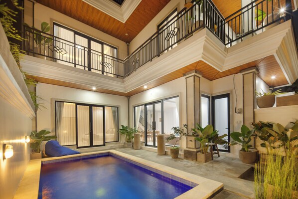 A multi-level indoor swimming pool area with a wooden ceiling, multiple balconies, and potted plants.