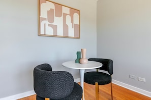 A room with a round table, two chairs, a vase, and a framed abstract artwork on the wall.