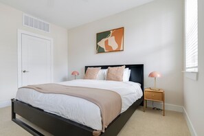 Un dormitorio con cama, mesitas de noche, una puerta, una ventana y una obra de arte colgada en la pared.