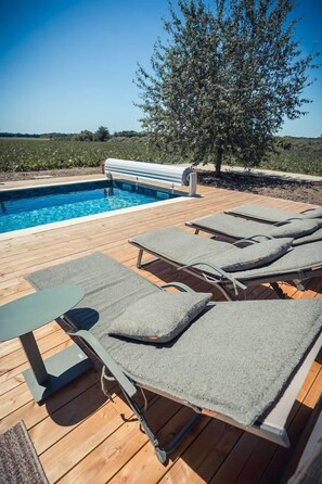 A poolside area with lounge chairs and a table, surrounded by a wooden deck and a tree. - Au Bout du Chemin Ecolodge (GERAUDOT)