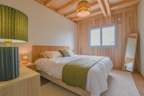 A bedroom with a wooden ceiling, a bed with white bedding, a bedside lamp, a window, and a mirror. - Au Bout du Chemin Ecolodge (GERAUDOT)