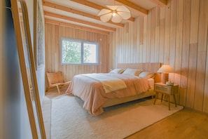 A bedroom with a bed, a chair, a nightstand, a lamp, and a window. - Au Bout du Chemin Ecolodge (GERAUDOT)