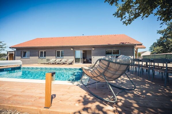 A modern house with a swimming pool, a wooden deck, and a chair. - Au Bout du Chemin Ecolodge (GERAUDOT)