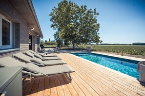 A wooden deck with a swimming pool, lounge chairs, and a large tree. - Au Bout du Chemin Ecolodge (GERAUDOT)