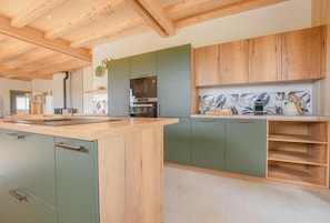 A modern kitchen with wooden beams, green cabinets, and a marble backsplash. - Au Bout du Chemin Ecolodge (GERAUDOT)
