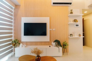 Un salón moderno con un televisor de pantalla plana montado en la pared, un mueble de entretenimiento blanco y suelo de madera.
