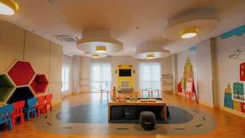 A spacious room with a central play area, multiple windows, and a colorful wall mural.