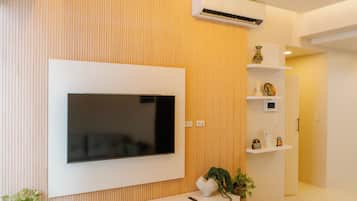 A modern living room with a flat-screen TV mounted on a white wall, a wooden floor, and a ceiling with recessed lighting.