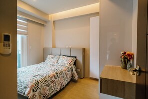 Ein Schlafzimmer mit einem Bett, einem Nachttisch mit Blumenvase, einem an der Wand montierten Thermostat und einer Tür mit Griff.