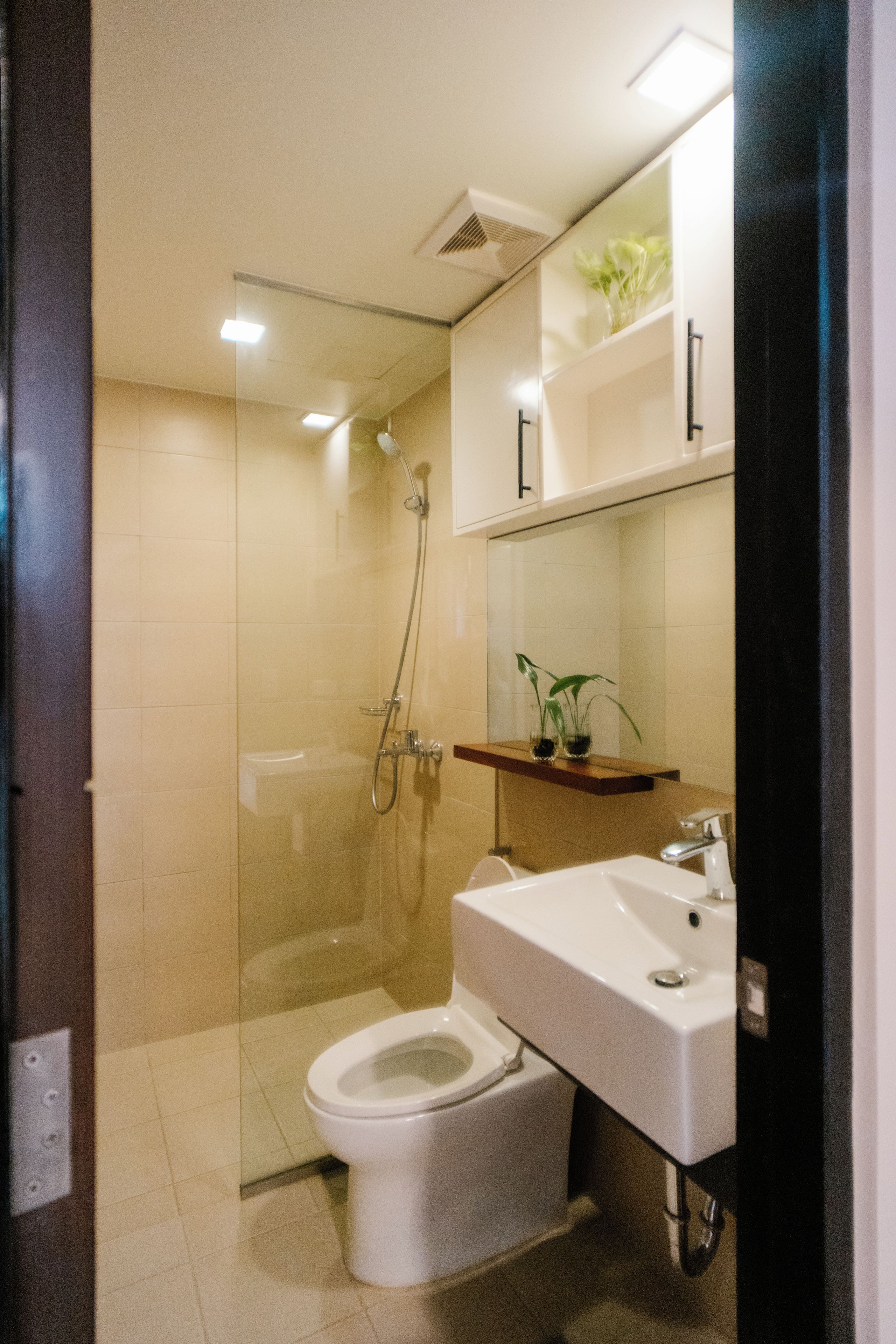 Un baño moderno con cabina de ducha de vidrio, un inodoro blanco y un lavabo con espejo superior.