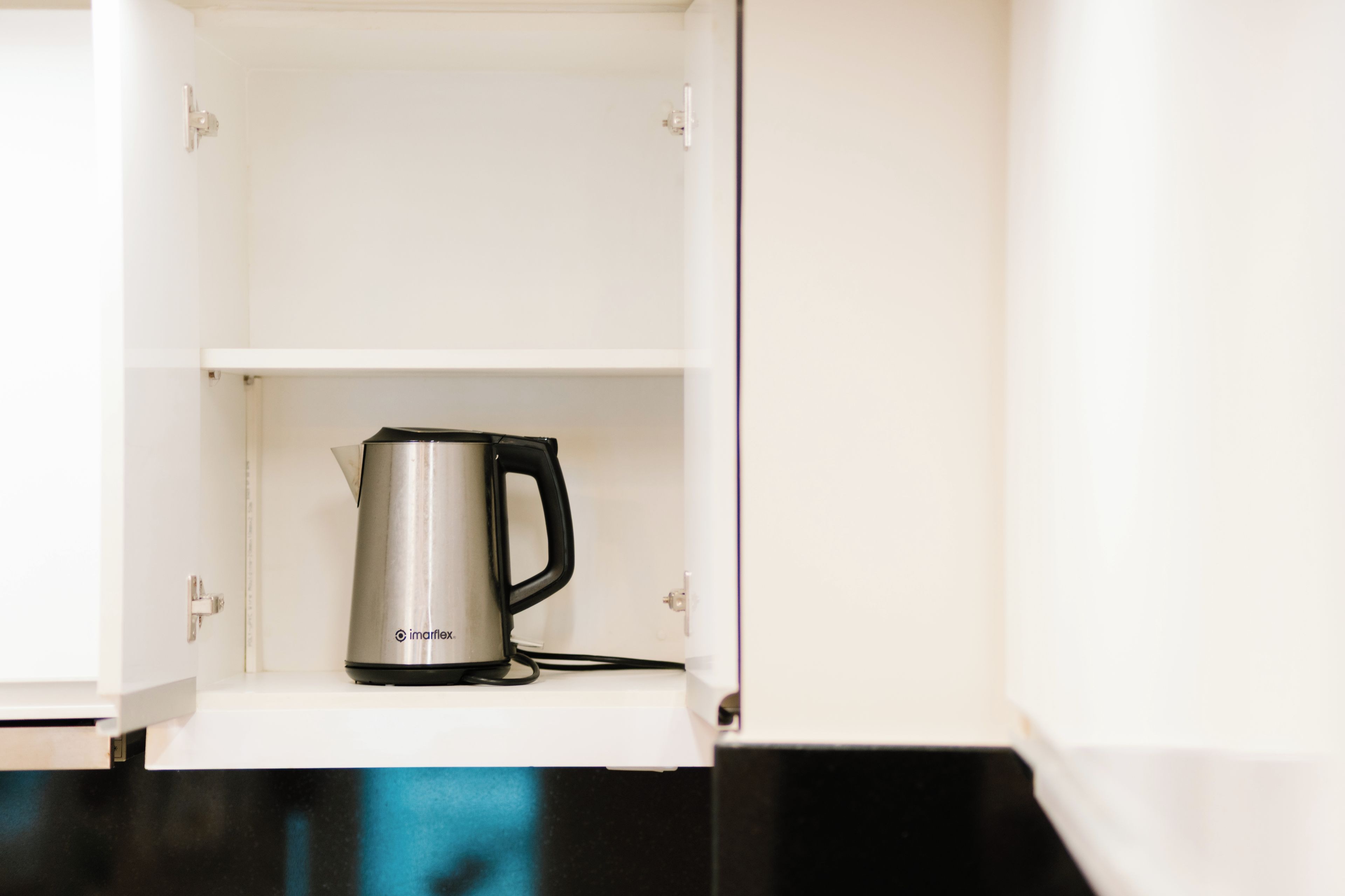 A white cabinet with a stainless steel electric kettle on the shelf.